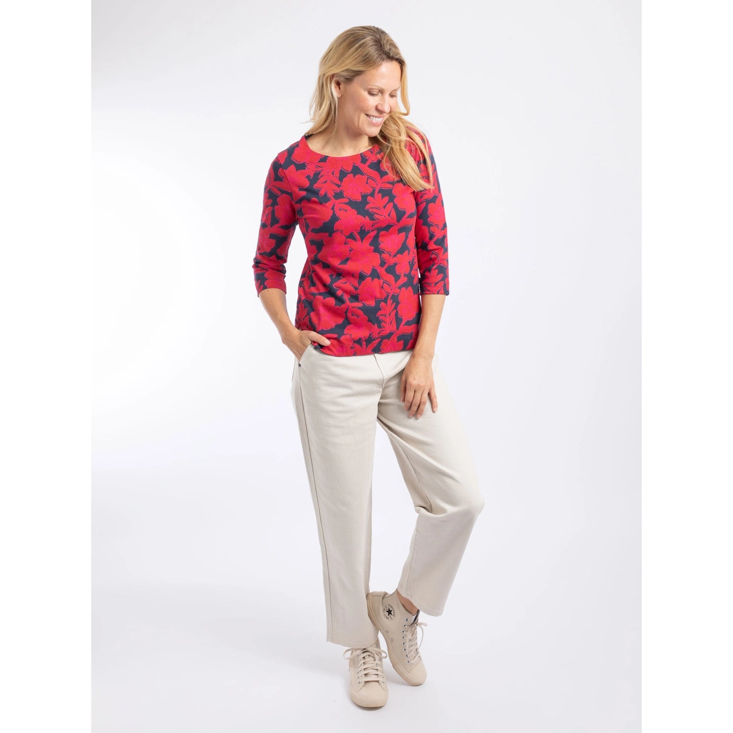 A woman wearing a Weird Fish three-quarter sleeve Pinto t-shirt in Cranberry Red with a bold floral pattern with cream trousers.