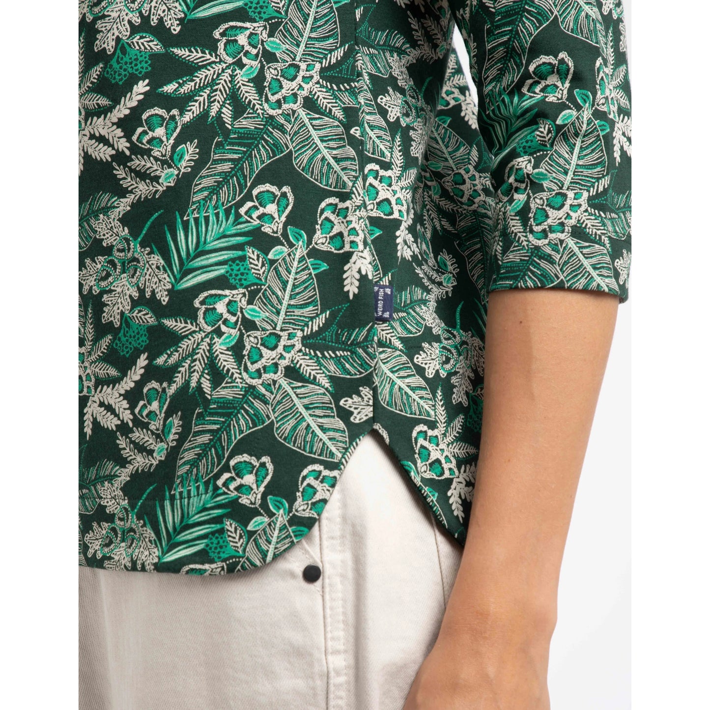 Close-up view of the curved side seam of a women's Weird Fish three-quarter sleeve Pinto t-shirt in Laurel Green with a leafy floral pattern.