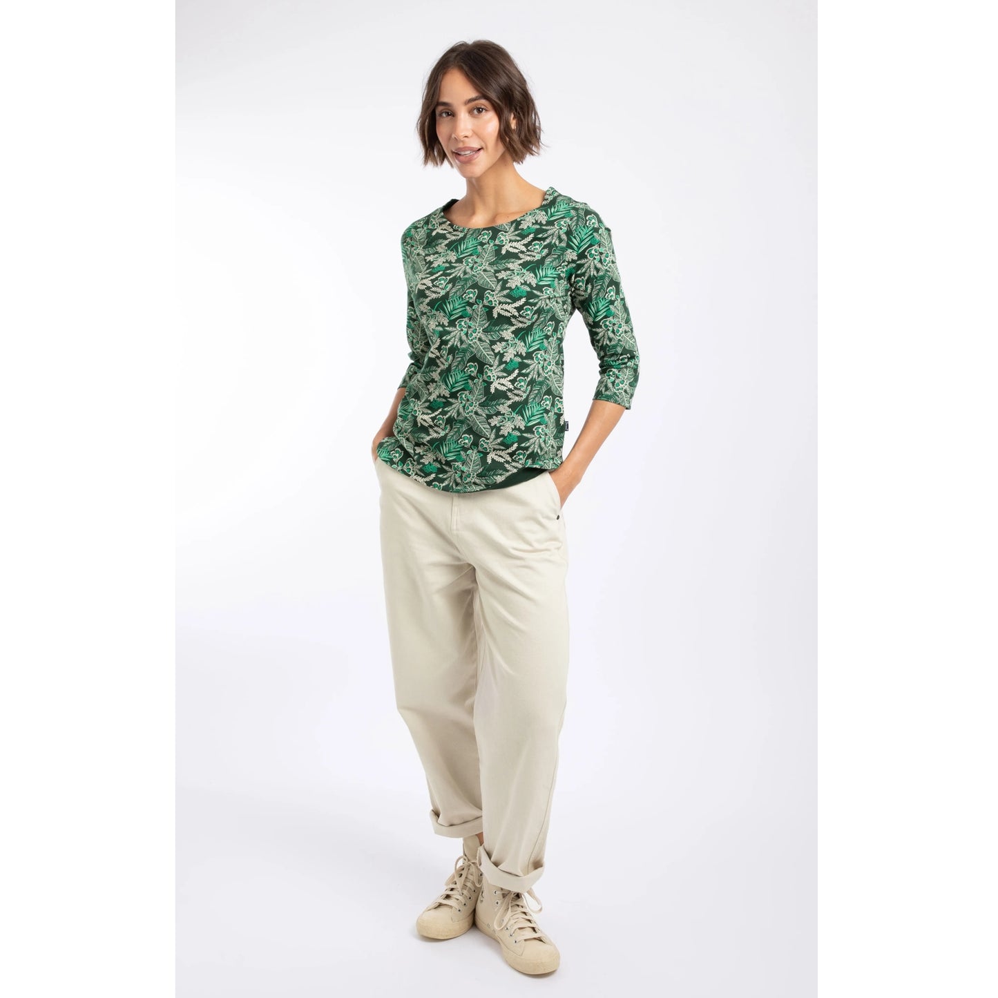 A woman wearing a Weird Fish three-quarter sleeve Pinto t-shirt in Laurel Green with a leafy floral pattern with cream trousers.