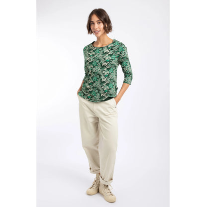 A woman wearing a Weird Fish three-quarter sleeve Pinto t-shirt in Laurel Green with a leafy floral pattern with cream trousers.