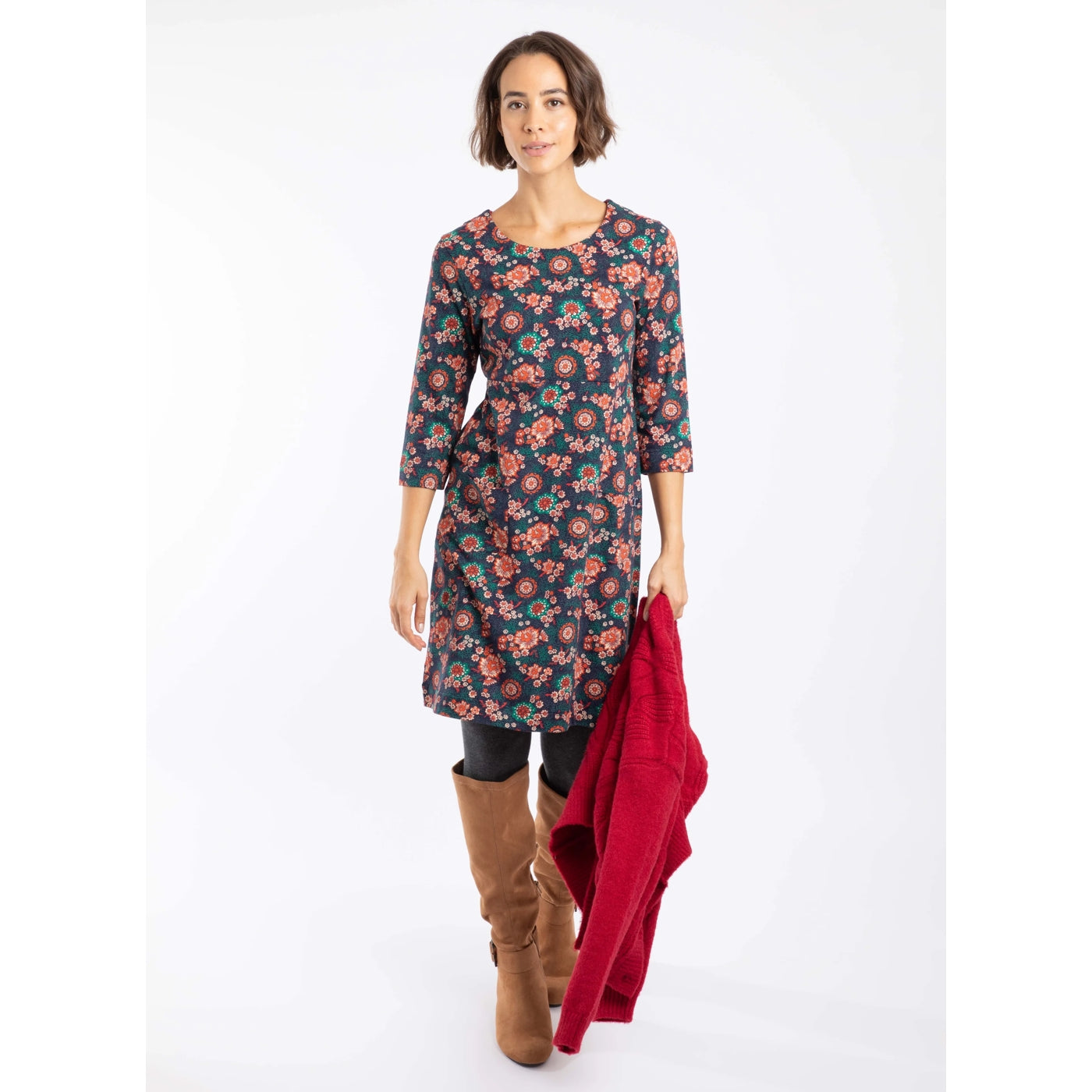 Woman wearing a Weird Fish dark blue and coral floral Starshine dress with a red jacket on a white background