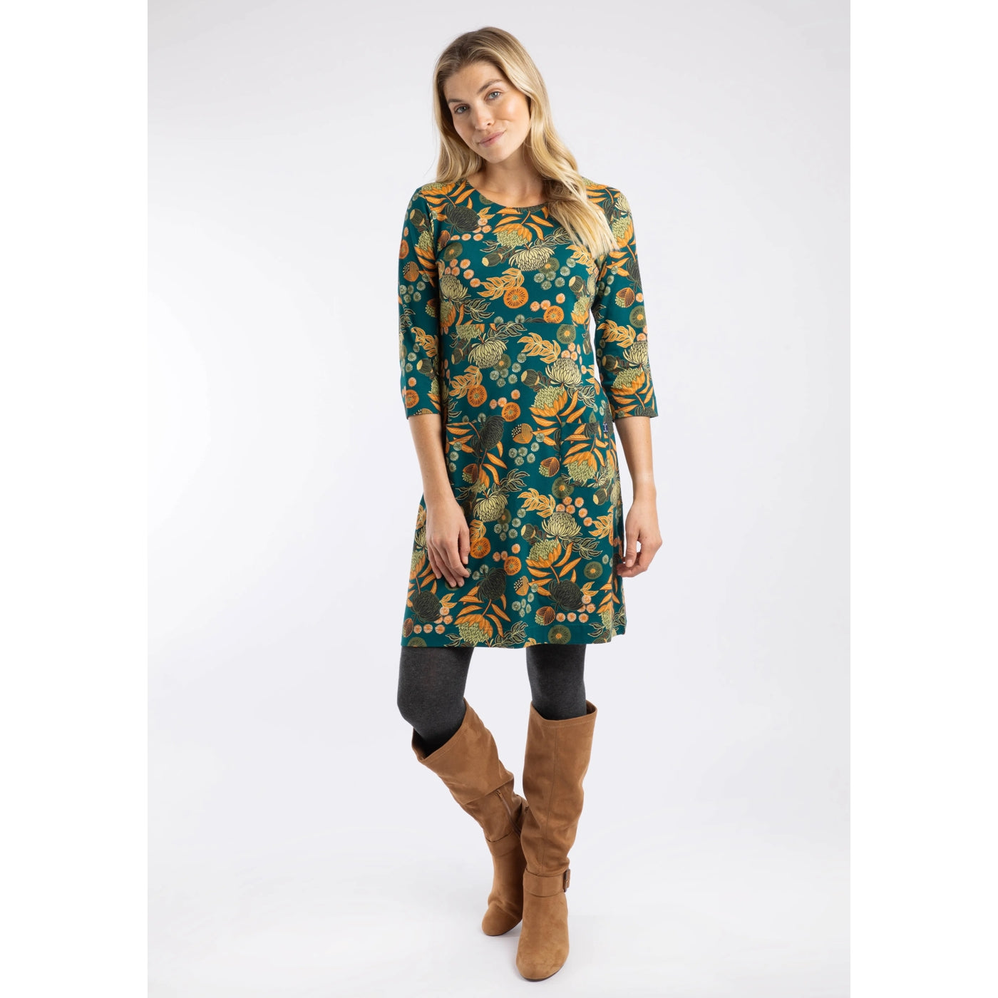 Woman wearing a Weird Fish Starshine Deep Teal floral patterned dress and brown boots on a white background