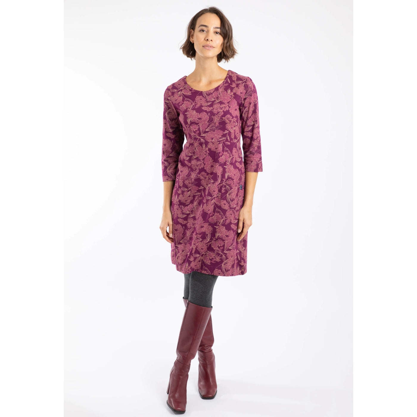Woman wearing a Weird Fish Plum purple floral patterned Starshine dress with long sleeves on a white background