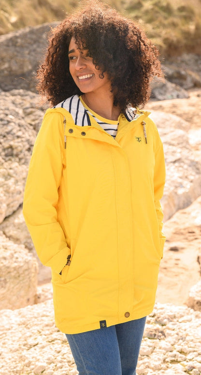 Lighthouse yellow waterproof jacket womens worn by smiling model outdoors on rocky background
